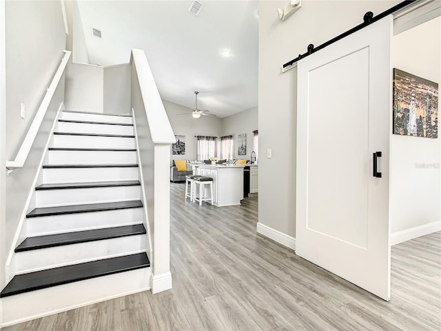 stairway featuring a barn door, ceiling fan, and light hardwood / wood-style flooring