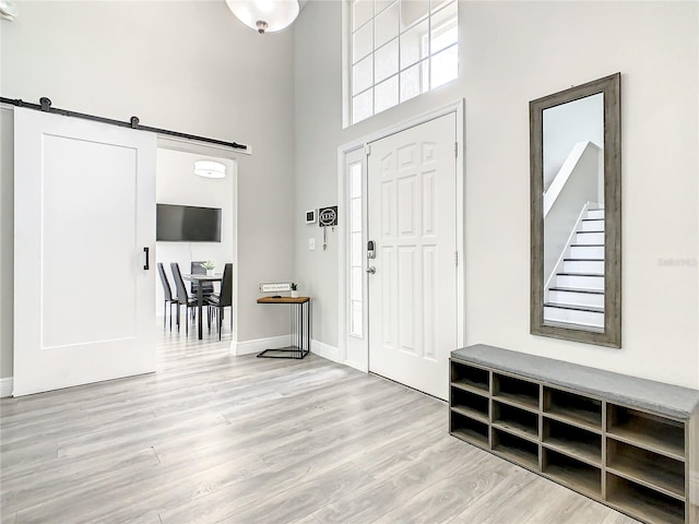 foyer with a barn door, light hardwood / wood-style floors, and a towering ceiling