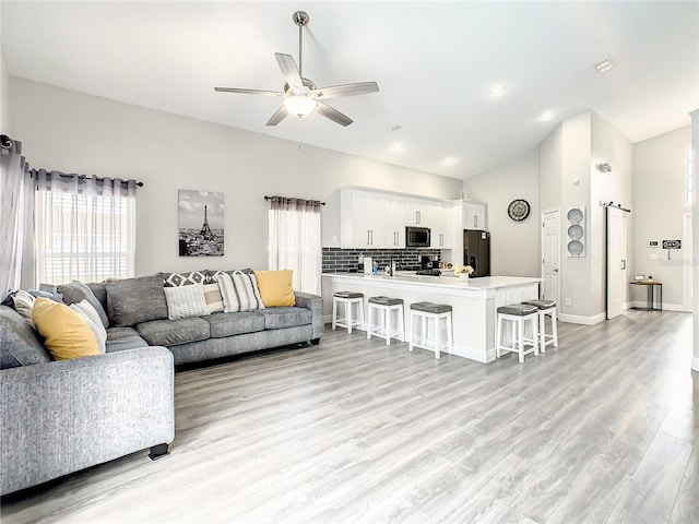 living room featuring a barn door, ceiling fan, vaulted ceiling, and light wood-type flooring