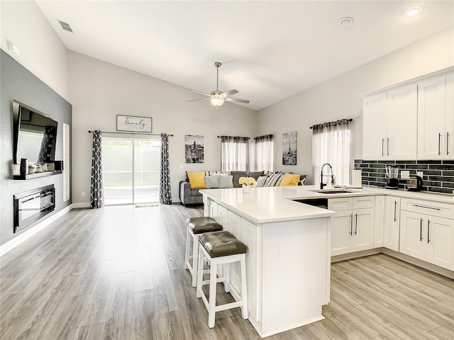 kitchen with ceiling fan, light wood-type flooring, white cabinets, backsplash, and lofted ceiling