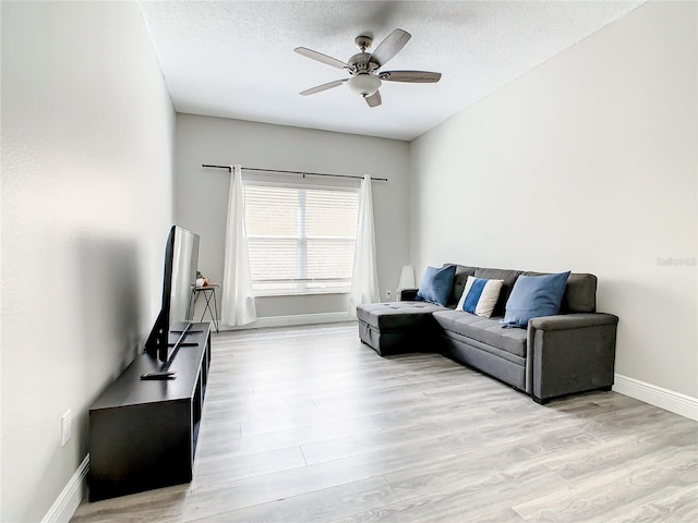 living room with a textured ceiling, ceiling fan, and light hardwood / wood-style flooring