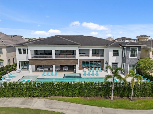 back of property featuring a balcony, a pool with hot tub, and a patio area