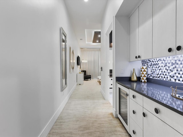 hallway with a raised ceiling, light colored carpet, and beverage cooler