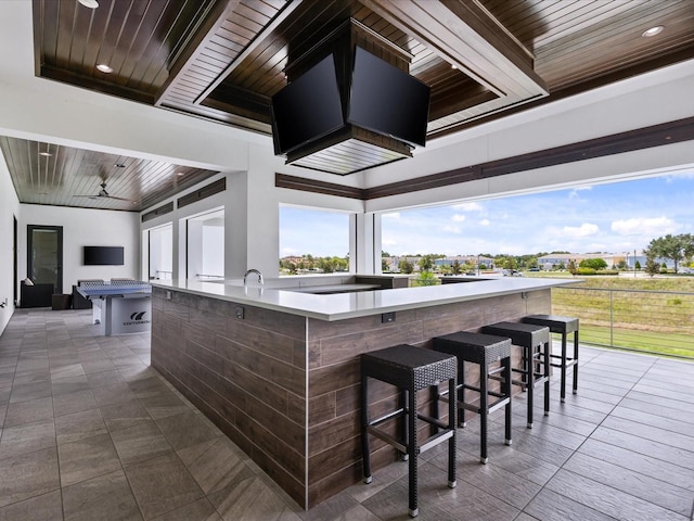 interior space featuring ceiling fan, wood ceiling, a kitchen island, dark tile flooring, and a breakfast bar area