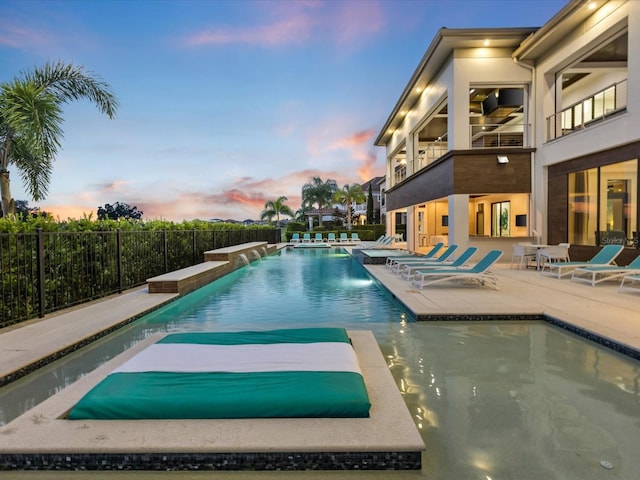 pool at dusk with a patio area and pool water feature