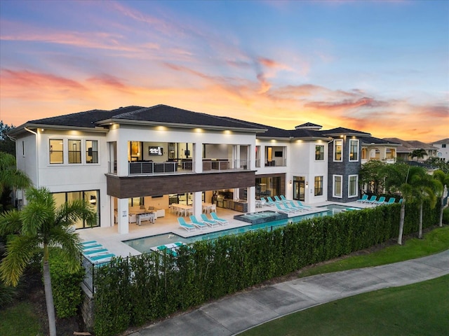 back house at dusk with a balcony, a patio area, and a fenced in pool