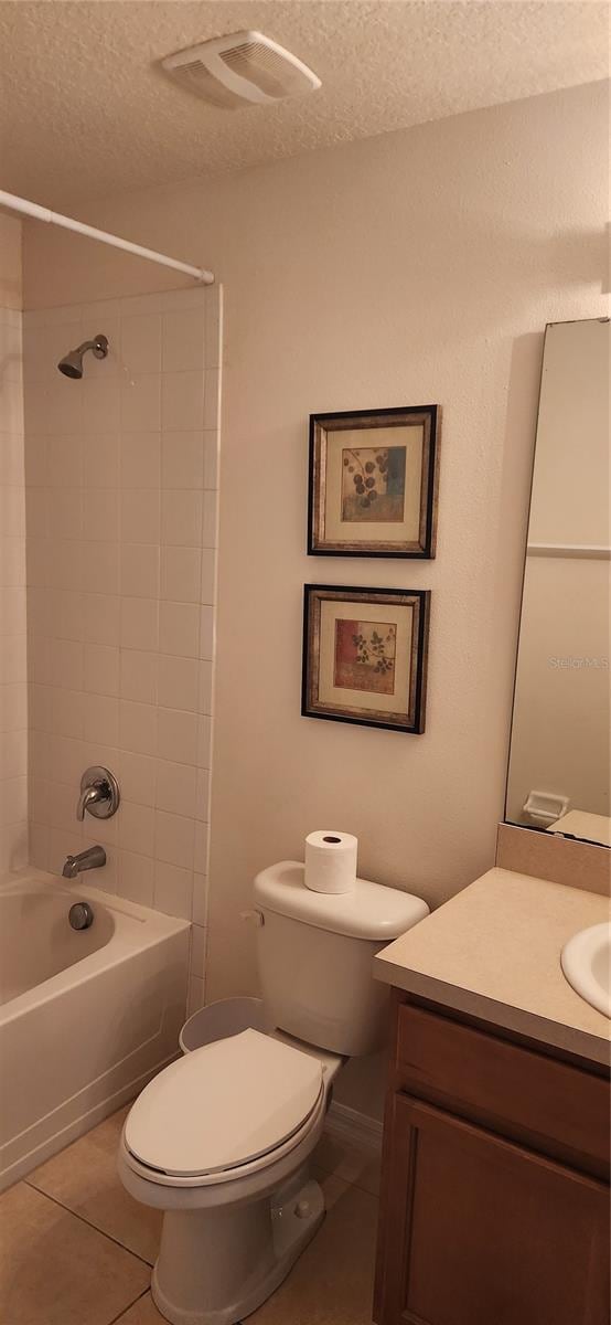 full bathroom featuring toilet, tiled shower / bath combo, vanity, a textured ceiling, and tile floors