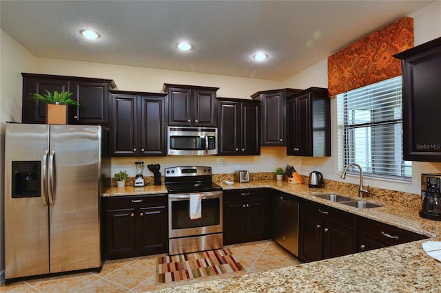 kitchen with sink, light tile floors, appliances with stainless steel finishes, light stone countertops, and dark brown cabinetry