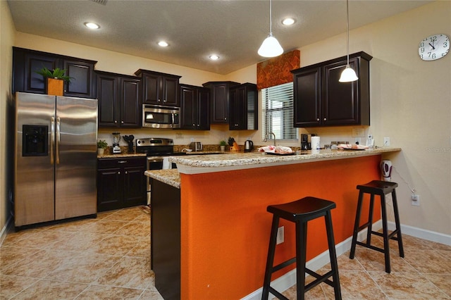 kitchen featuring light tile floors, decorative light fixtures, a kitchen bar, light stone countertops, and appliances with stainless steel finishes