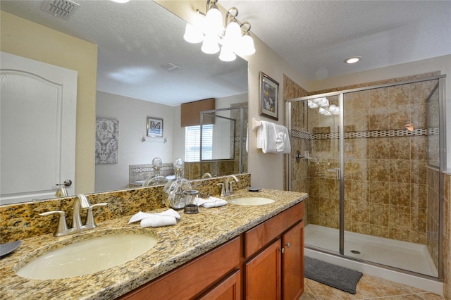 bathroom featuring an inviting chandelier, double sink vanity, tile floors, a shower with door, and a textured ceiling