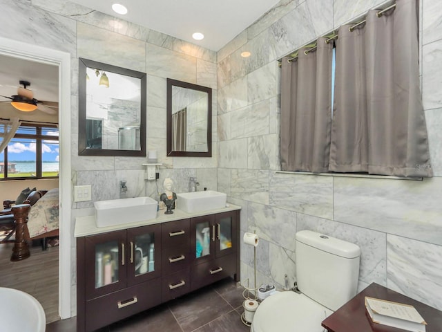 bathroom with tile walls, toilet, ceiling fan, double sink vanity, and tile floors