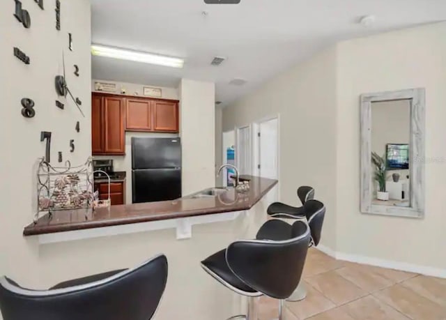 kitchen featuring light tile floors, sink, a kitchen bar, and stainless steel refrigerator