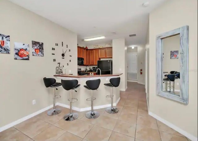 kitchen featuring a breakfast bar, light tile floors, and black appliances