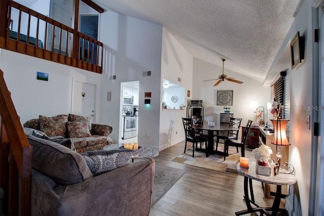 living room featuring ceiling fan, high vaulted ceiling, light hardwood / wood-style floors, and a textured ceiling