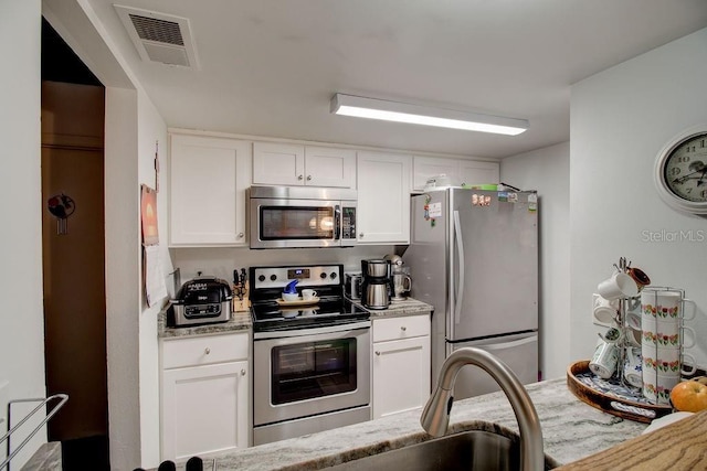 kitchen featuring white cabinets, appliances with stainless steel finishes, and light stone counters