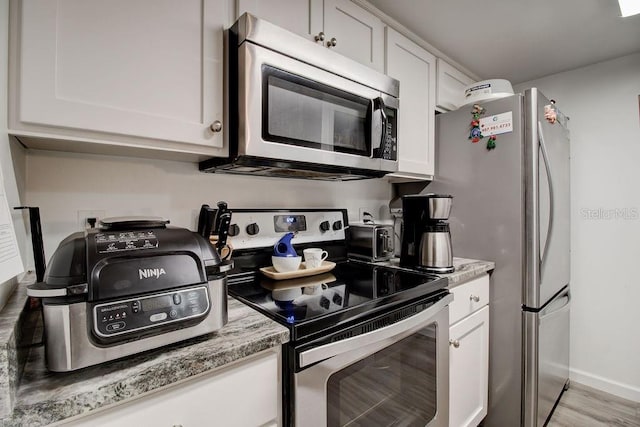 kitchen featuring light stone counters, white cabinetry, appliances with stainless steel finishes, and light hardwood / wood-style flooring