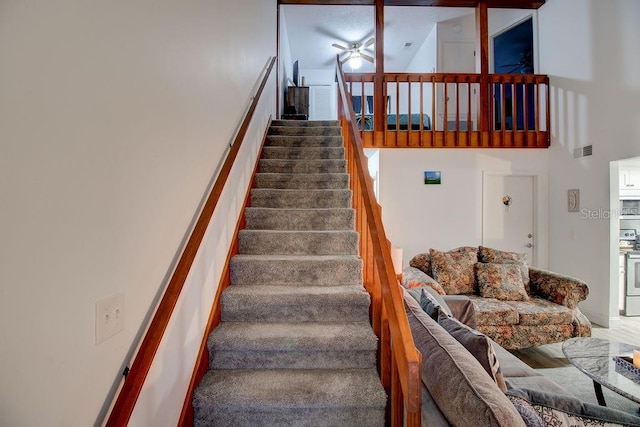 stairs with ceiling fan and a high ceiling