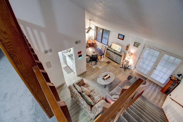 living room featuring a high ceiling, french doors, ceiling fan, a textured ceiling, and light hardwood / wood-style floors