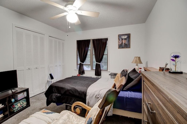 bedroom with a textured ceiling, carpet floors, ceiling fan, and multiple closets