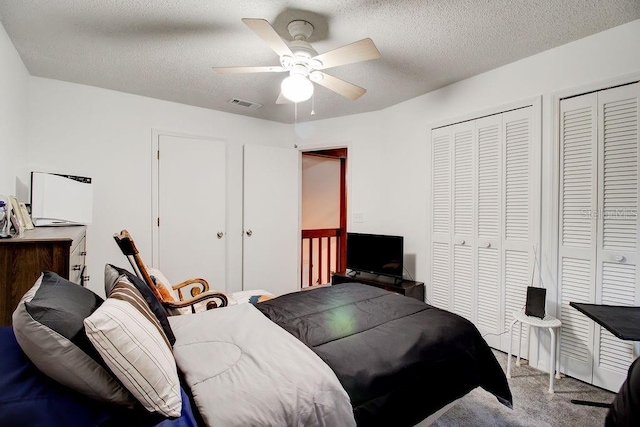 carpeted bedroom featuring ceiling fan, a textured ceiling, and two closets