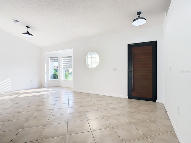 spare room with lofted ceiling, a textured ceiling, and light tile patterned flooring