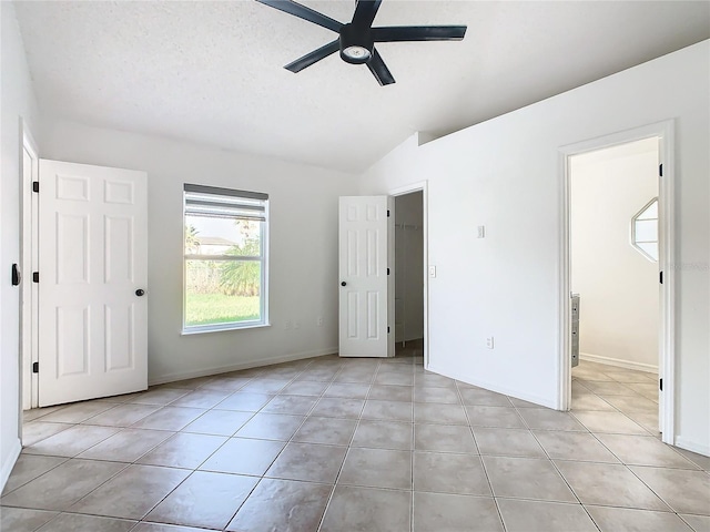 unfurnished bedroom with a spacious closet, vaulted ceiling, light tile patterned floors, a textured ceiling, and ceiling fan