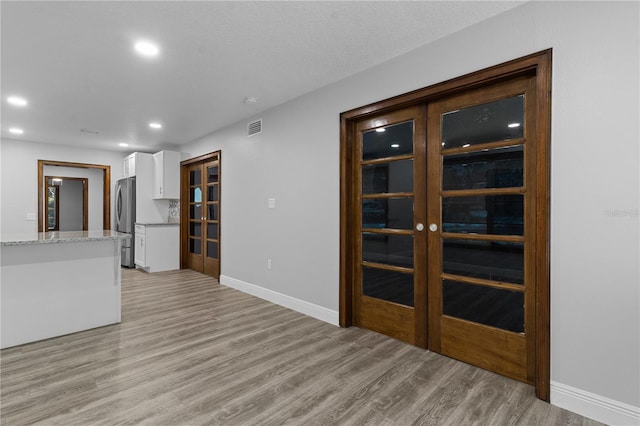 interior space with light stone counters, stainless steel refrigerator, white cabinetry, and light hardwood / wood-style flooring