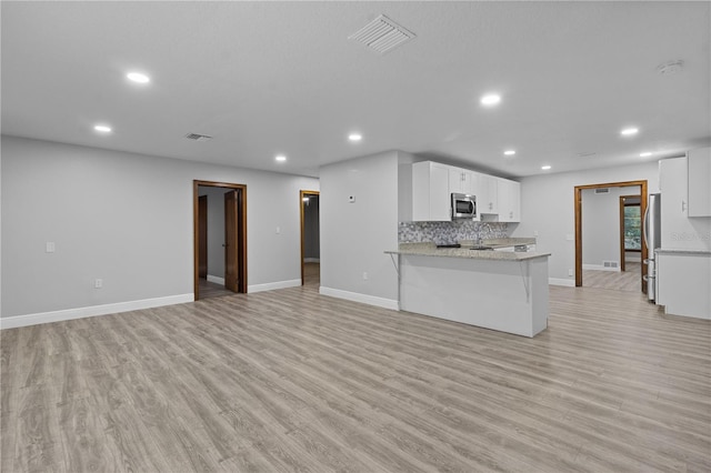 kitchen featuring light stone counters, appliances with stainless steel finishes, backsplash, light hardwood / wood-style floors, and white cabinetry