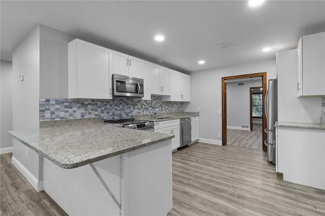 kitchen featuring appliances with stainless steel finishes, light hardwood / wood-style flooring, white cabinets, light stone counters, and tasteful backsplash