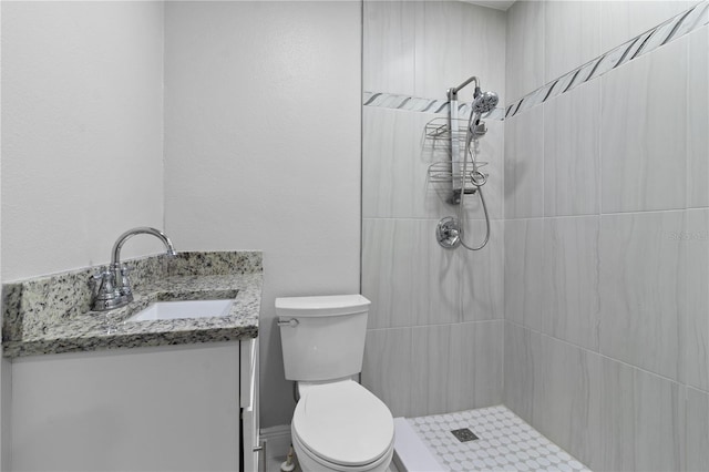 bathroom featuring toilet, a tile shower, and vanity