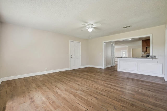 unfurnished living room featuring ceiling fan, a textured ceiling, and dark wood-type flooring