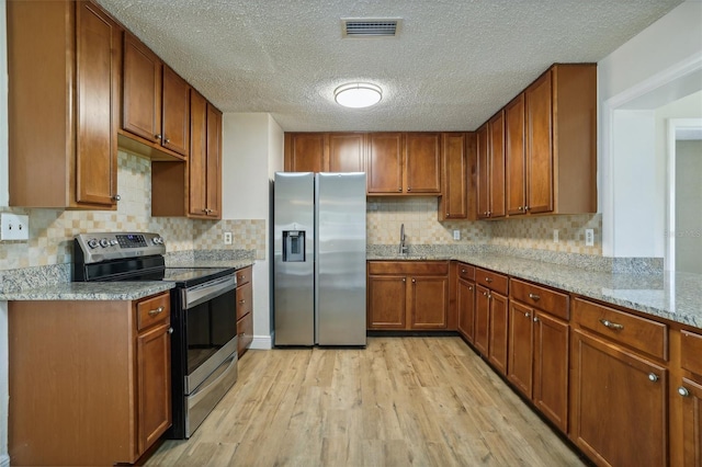 kitchen featuring light stone counters, backsplash, appliances with stainless steel finishes, and light wood-type flooring