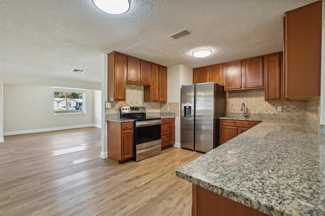 kitchen featuring appliances with stainless steel finishes, backsplash, a textured ceiling, light hardwood / wood-style flooring, and sink