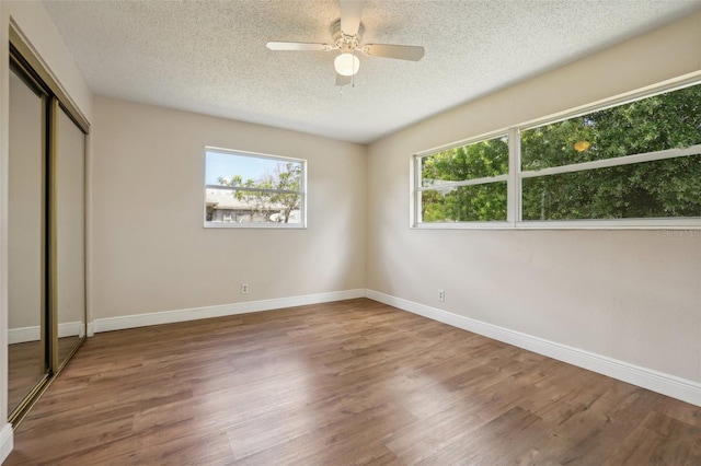 unfurnished bedroom featuring ceiling fan, a textured ceiling, a closet, and hardwood / wood-style floors