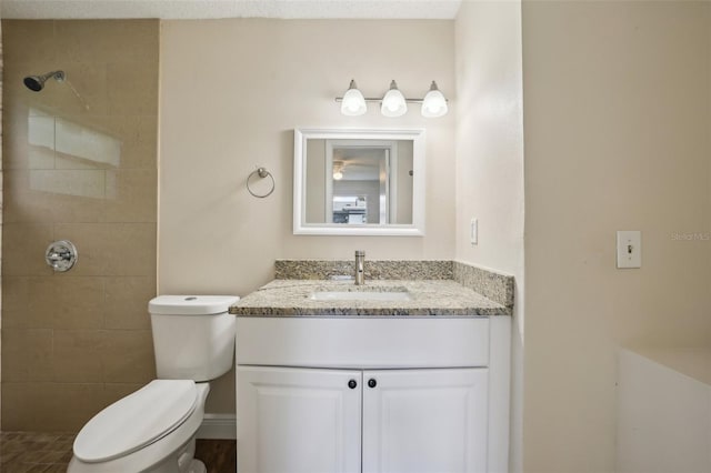 bathroom featuring a textured ceiling, tiled shower, vanity, and toilet