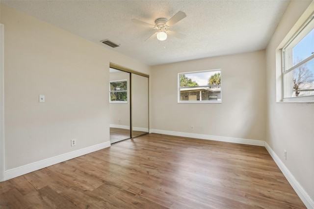 unfurnished bedroom with a textured ceiling, wood-type flooring, ceiling fan, and a closet