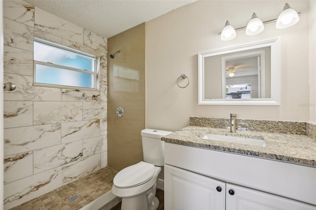 bathroom featuring a textured ceiling, a tile shower, vanity, and toilet