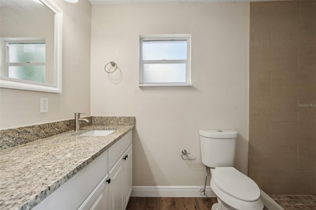 bathroom with tiled shower, hardwood / wood-style flooring, vanity, and toilet