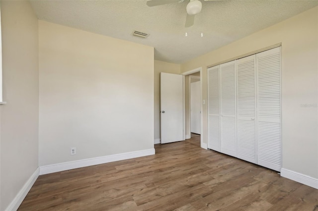 unfurnished bedroom featuring ceiling fan, a textured ceiling, a closet, and wood-type flooring