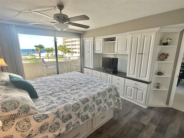 bedroom with ceiling fan, access to outside, dark wood-type flooring, a water view, and a textured ceiling