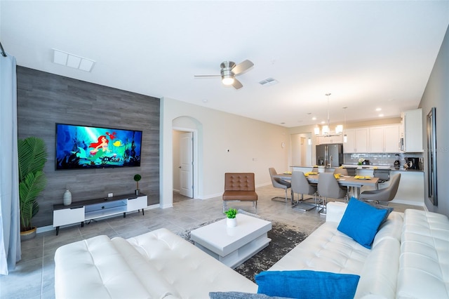 tiled living room featuring tile walls and ceiling fan with notable chandelier