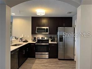 kitchen with appliances with stainless steel finishes, sink, dark brown cabinetry, and light hardwood / wood-style flooring