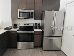 kitchen with appliances with stainless steel finishes, dark brown cabinets, and light hardwood / wood-style flooring