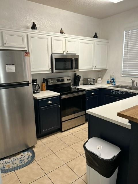 kitchen with sink, light tile patterned flooring, a textured ceiling, white cabinets, and appliances with stainless steel finishes