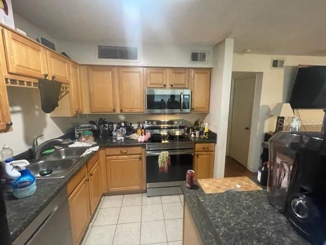 kitchen with dark stone countertops, sink, light tile patterned floors, and stainless steel appliances