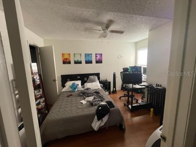 bedroom with hardwood / wood-style floors, ceiling fan, and a textured ceiling