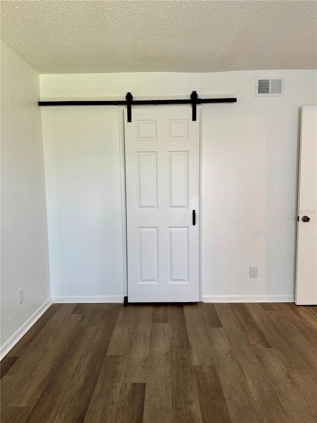 unfurnished bedroom featuring a textured ceiling, a closet, hardwood / wood-style flooring, and a barn door