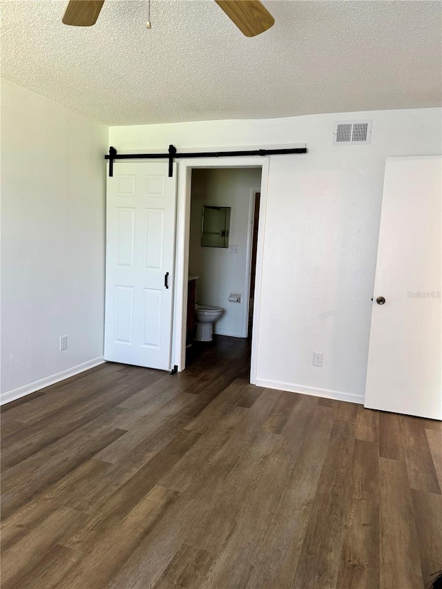 unfurnished bedroom with ceiling fan, hardwood / wood-style floors, a barn door, ensuite bath, and a textured ceiling