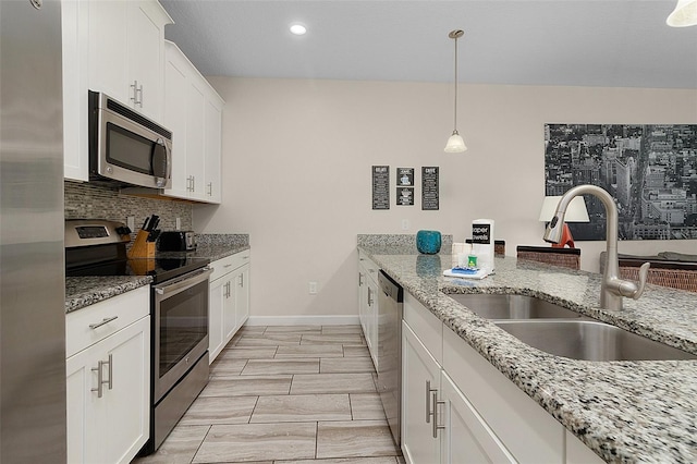 kitchen featuring sink, white cabinets, stainless steel appliances, light stone countertops, and decorative light fixtures