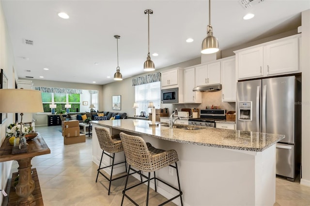 kitchen with decorative light fixtures, light stone countertops, a center island with sink, appliances with stainless steel finishes, and white cabinets